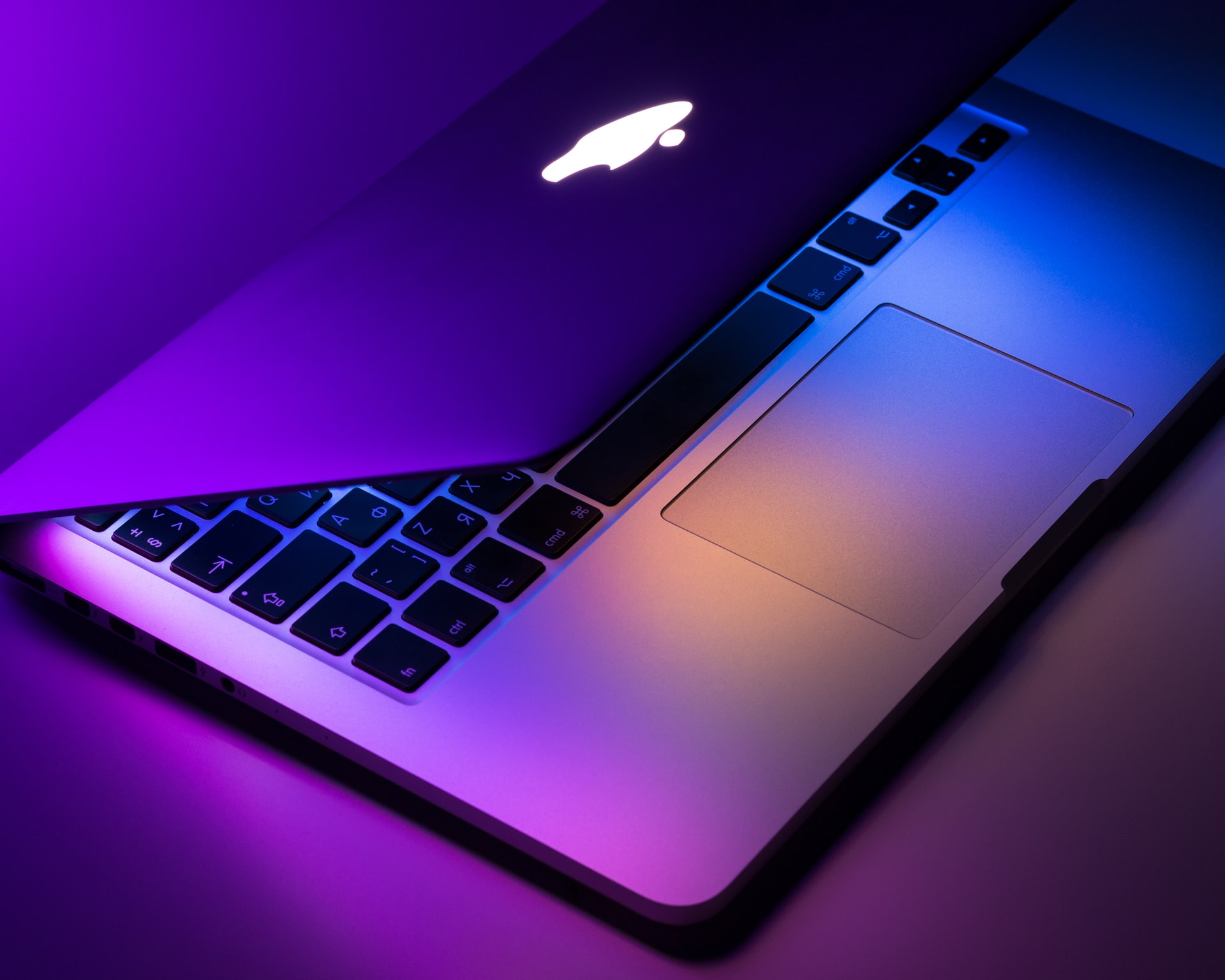 A silver MacBook opening its lid with ambient purple light.